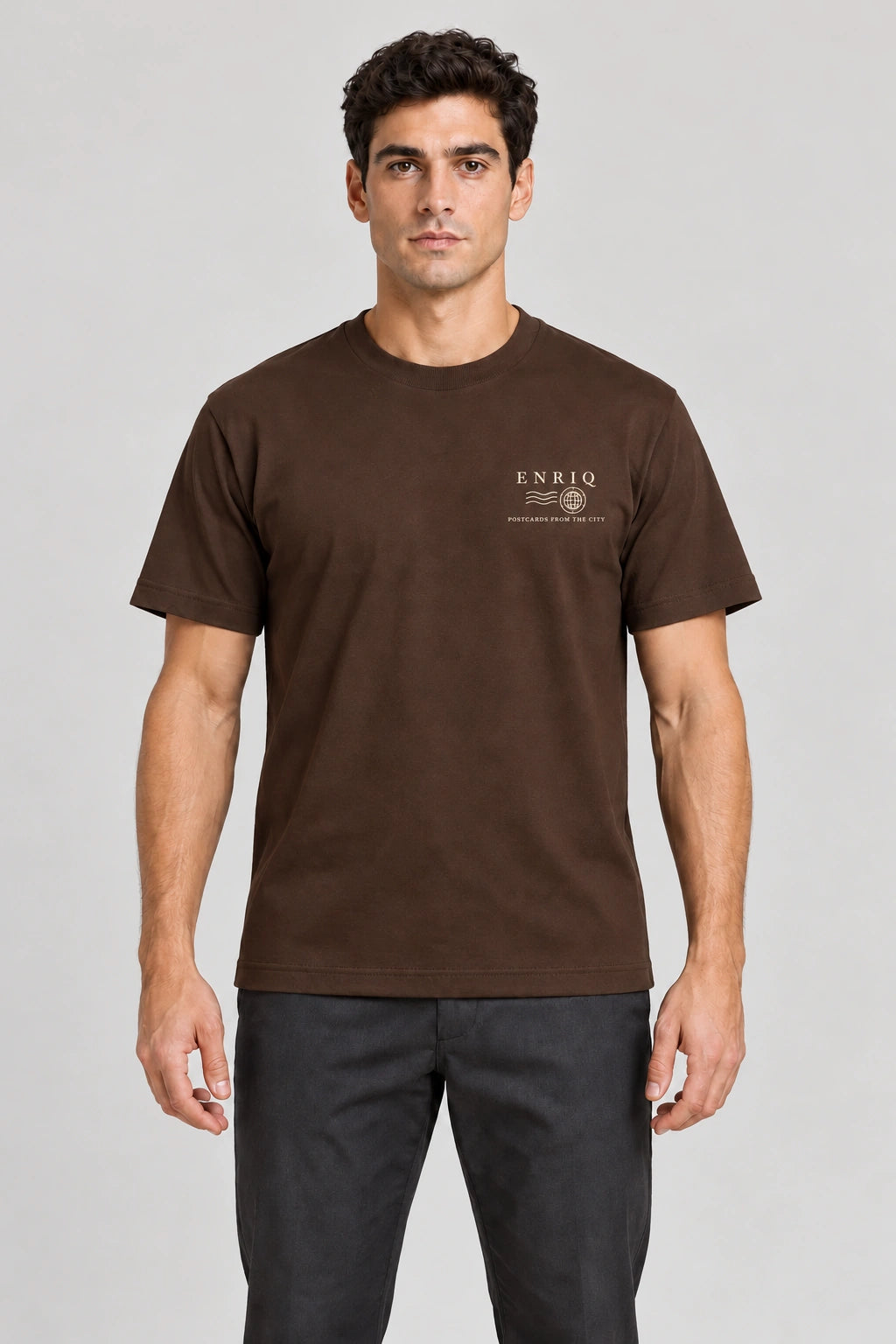 ENRIQ City Stamp Tee Cocoa – voorkant op model met ENRIQ poststempel-borstlogo (AI-visualisatie)