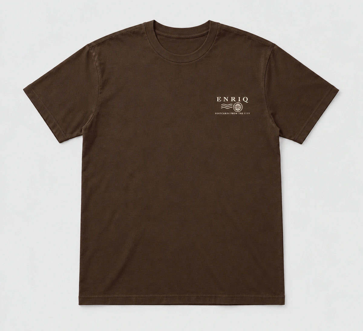 ENRIQ City Stamp Tee Cocoa – flatlay met ENRIQ poststempel-borstlogo (AI-visualisatie)