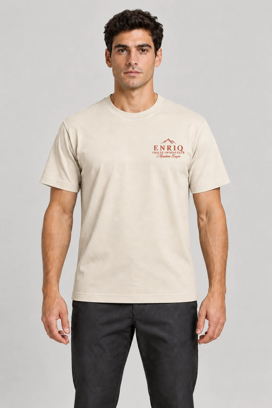 ENRIQ Chalet Owners Tee Bone – voorkant op model met bergtoppen en Chalet Owners Club borstlogo (AI-visualisatie)
