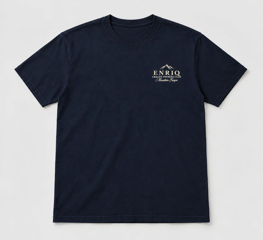 ENRIQ Chalet Owners Tee Navy – flatlay met bergtoppen en Chalet Owners Club borstlogo (AI-visualisatie)