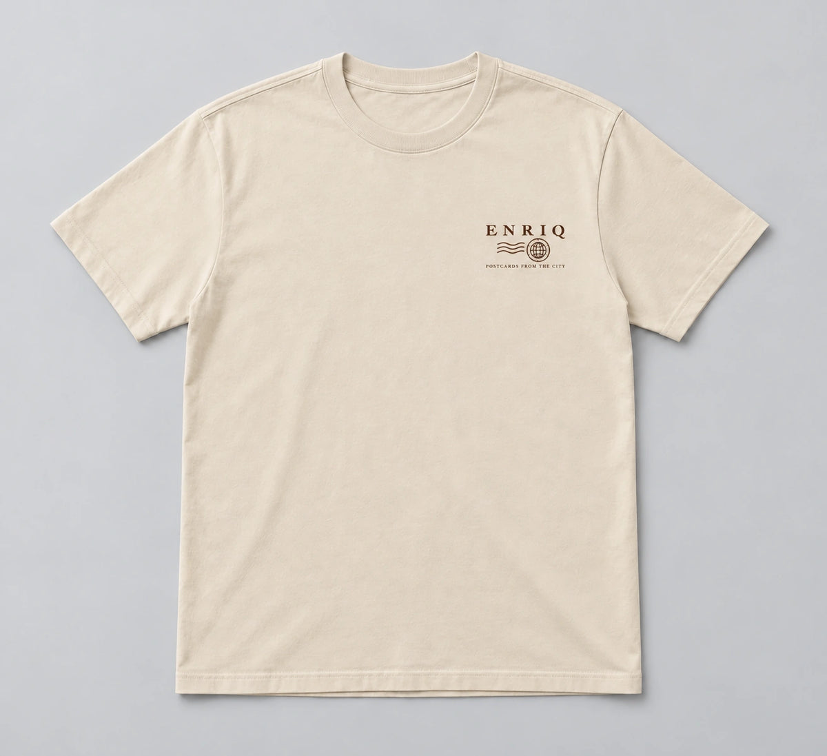 ENRIQ City Stamp Tee Bone – flatlay met ENRIQ poststempel-borstlogo (AI-visualisatie)