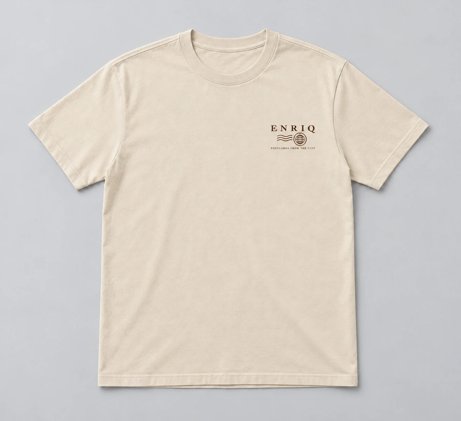 ENRIQ City Stamp Tee Bone – flatlay met ENRIQ poststempel-borstlogo (AI-visualisatie)