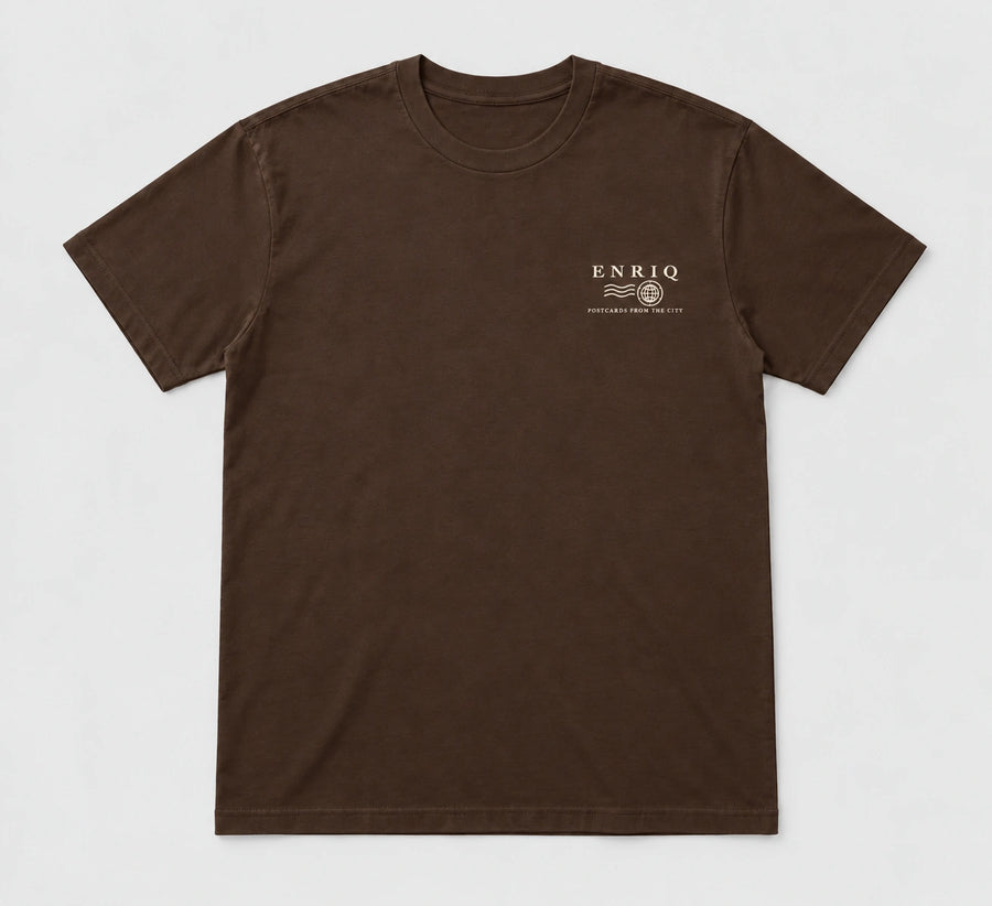 ENRIQ City Stamp Tee Cocoa – flatlay met ENRIQ poststempel-borstlogo (AI-visualisatie)